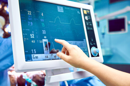 Monitoring Patient's Vital Sign In Operating Room. Doctor Cheking At Patient's Vital Signs. Cardiogram Monitor During Surgery In Operation Room.