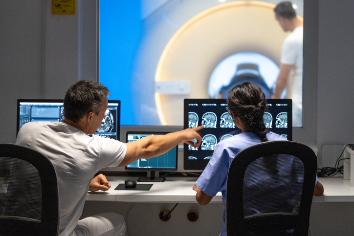 Two MRI Radiologists Sitting In The Control Room And Operating The MRI Scanner