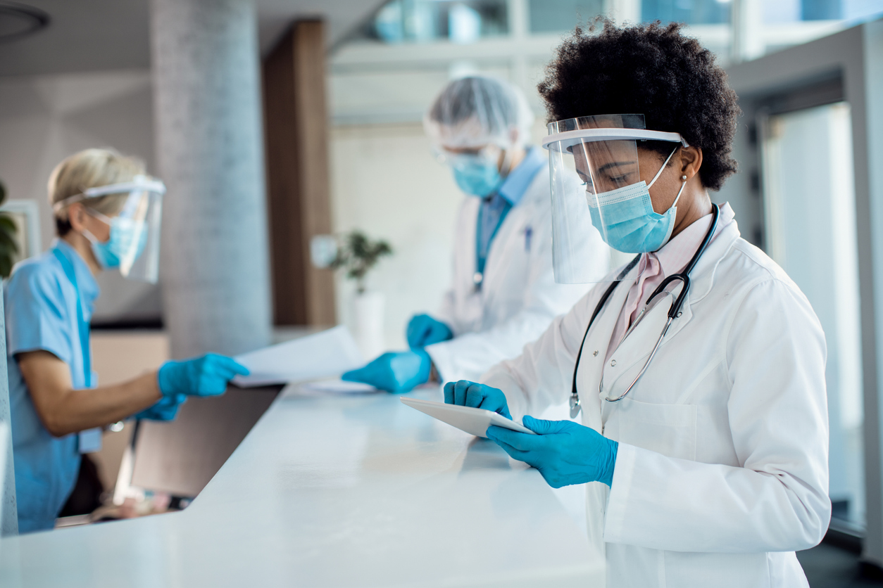 a doctor in a lab wearing a face mask and gloves while looking at a tablet