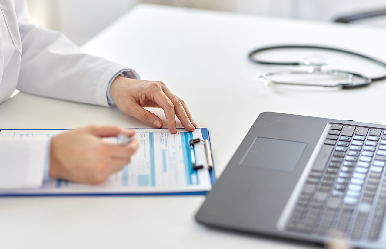 a doctor looking at a form on a clipboard in front of a laptop