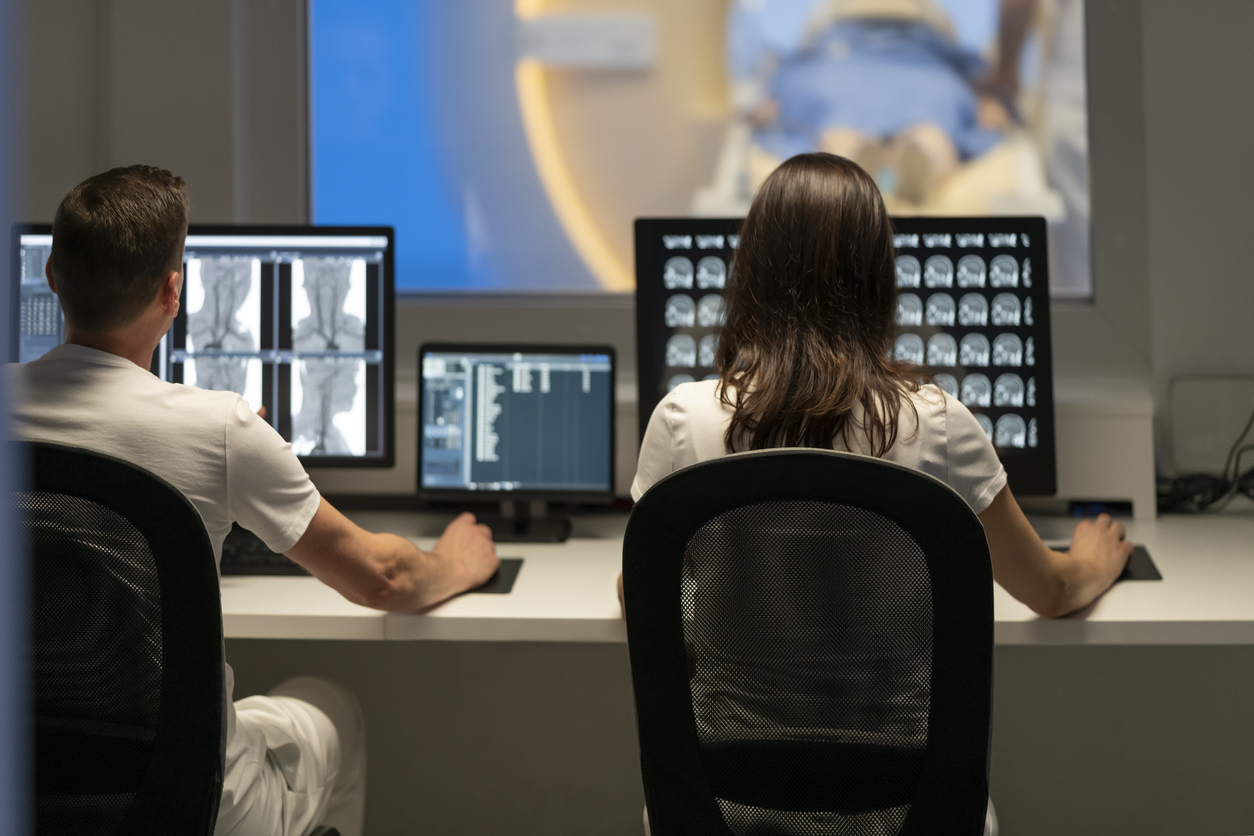 a woman looking at brain scans on a computer screen and a man looking at neck CT scans on a computer screen