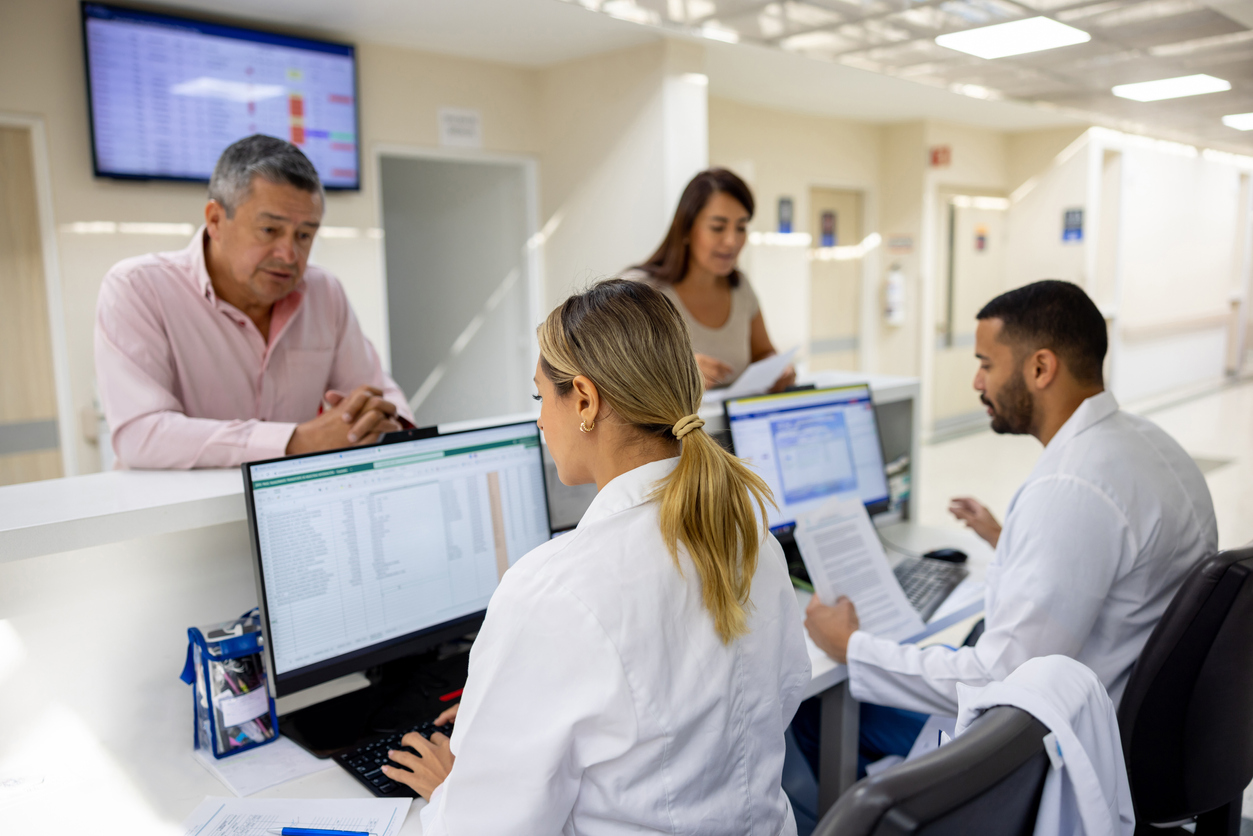 hospital employees looking at computers and talking to patients from behind a desk