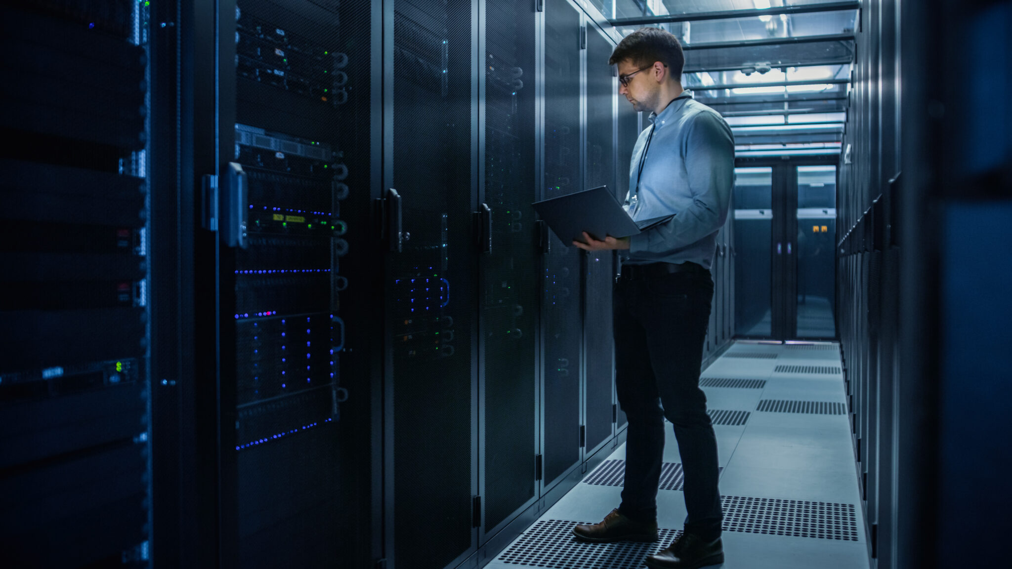 An IT administrator in a university server room monitoring network traffic and IoT device communications to ensure IoT device network segmentation and security on campus.