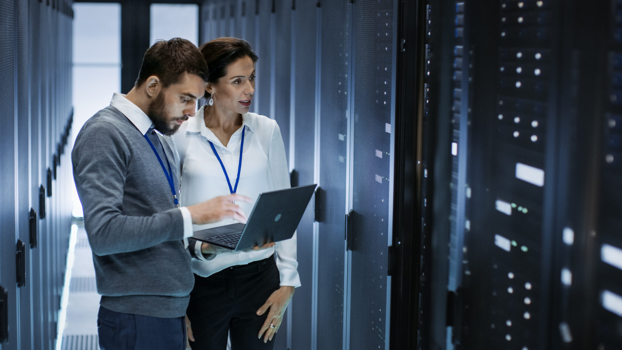 University IT administrators in a server room reviewing IoT device network activity, ensuring real-time monitoring and segmentation for cybersecurity with Cylera’s platform