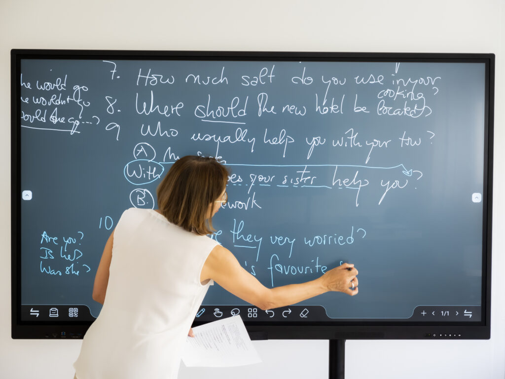 A teacher using a smart board in a higher education classroom, illustrating an IoT enabled interactive learning experience while the Cylera platform’s IoT threat detection ensures a secure campus network.