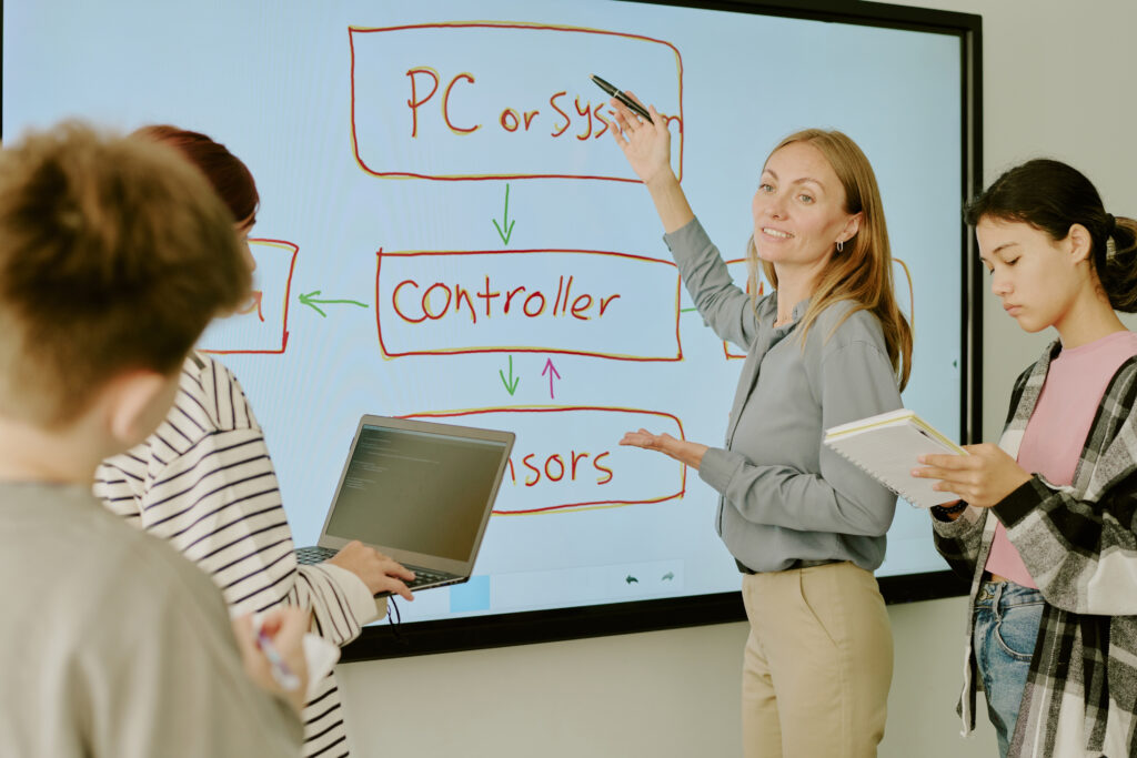 Higher education instructor using a smart board integrated with IoT technology to enhance interactive learning and improve student engagement in a classroom environment.