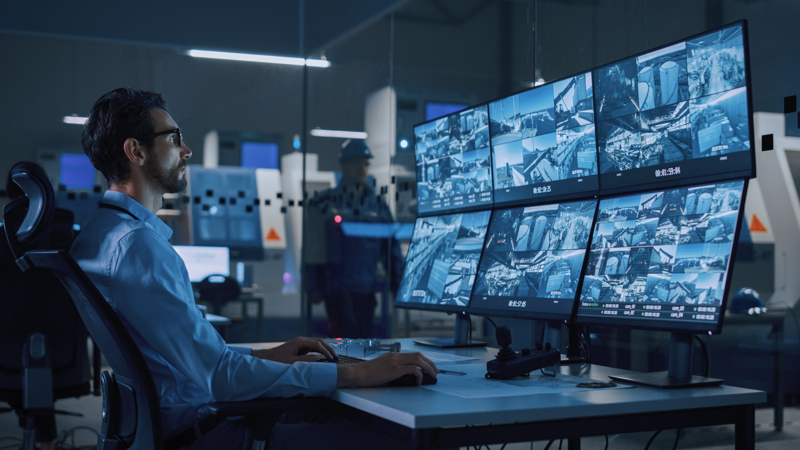 A cybersecurity professional monitoring multiple security camera feeds and network activity, using Cylera’s platform for real-time IoT device asset inventory, vulnerability and risk management, threat detection and response, and operational and security analytics across connected devices.