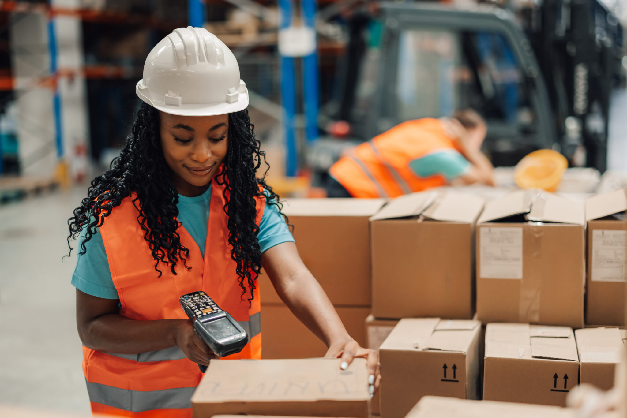 A transportation and logistics industry employee scanning boxes in a warehouse with a handheld IoT device scanner that the Cylera platform can discover and inventory for continuous IoT asset inventory visibility and security.